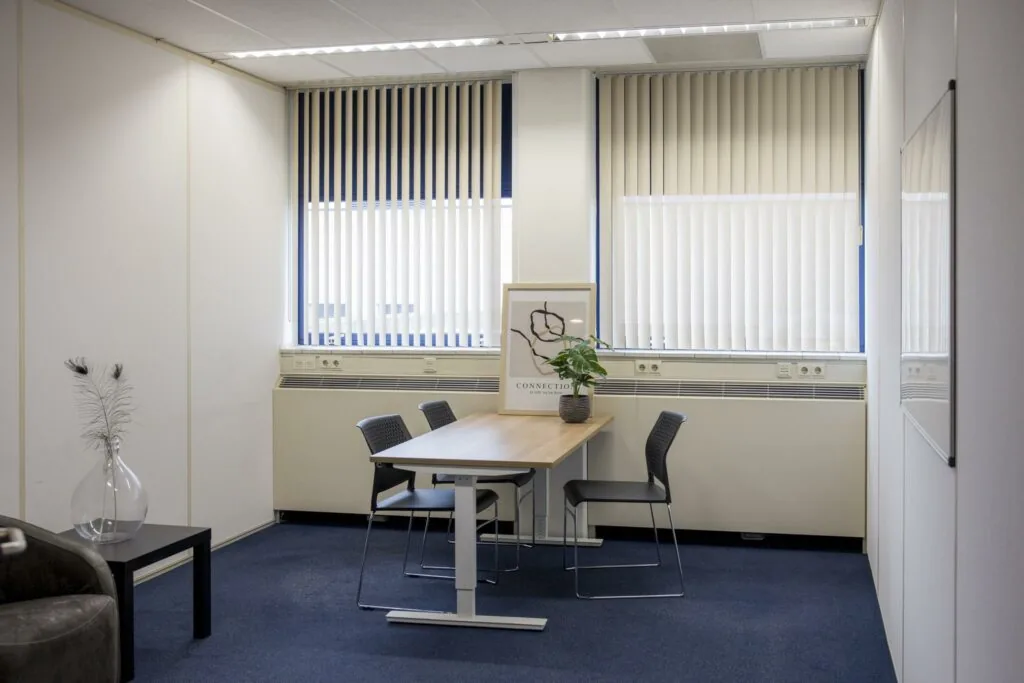 Vergaderruimte aan de Markerkant 13 met een tafel, vier stoelen, een plant en een kunstposter.